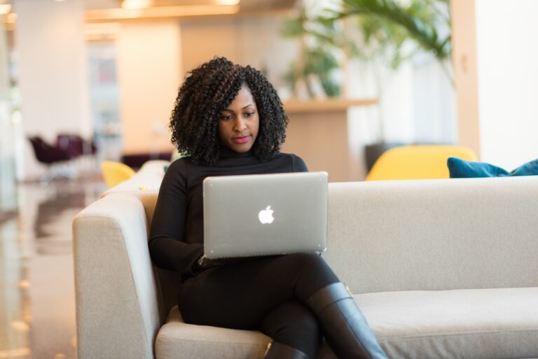 Black woman sitting on sofa working from laptop