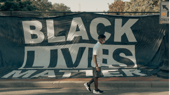 Man walking in front of Black Lives Matter flag