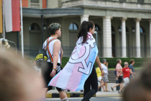Two people marching at Pride displaying the Trans flag