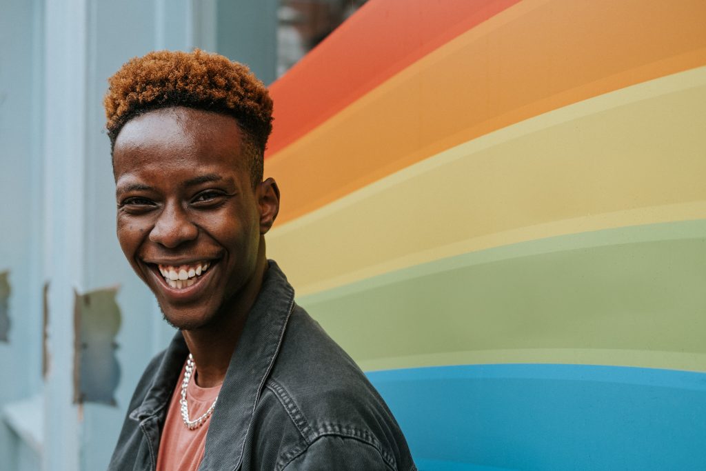 Black person smiling in front of LGBT+ flag