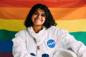 Person in an astronaut suit standing in front of LGBT flag
