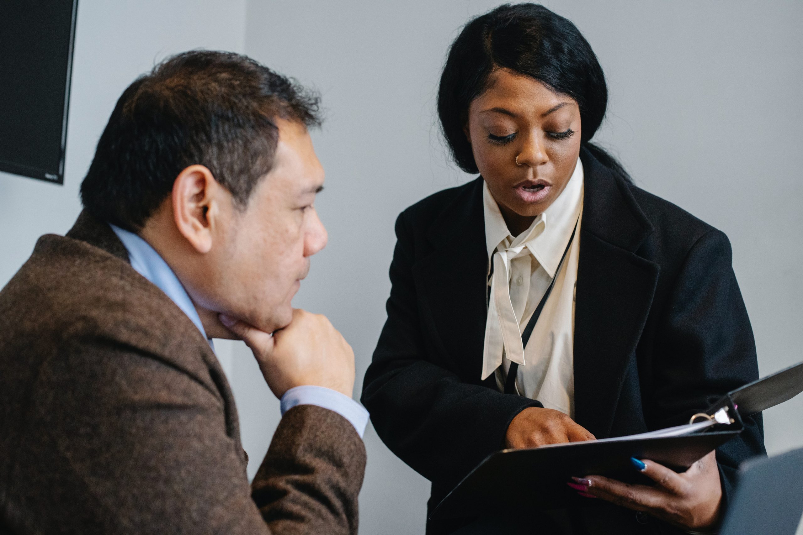 Line manager pointing at document in their binder, while their colleague listens to their briefing