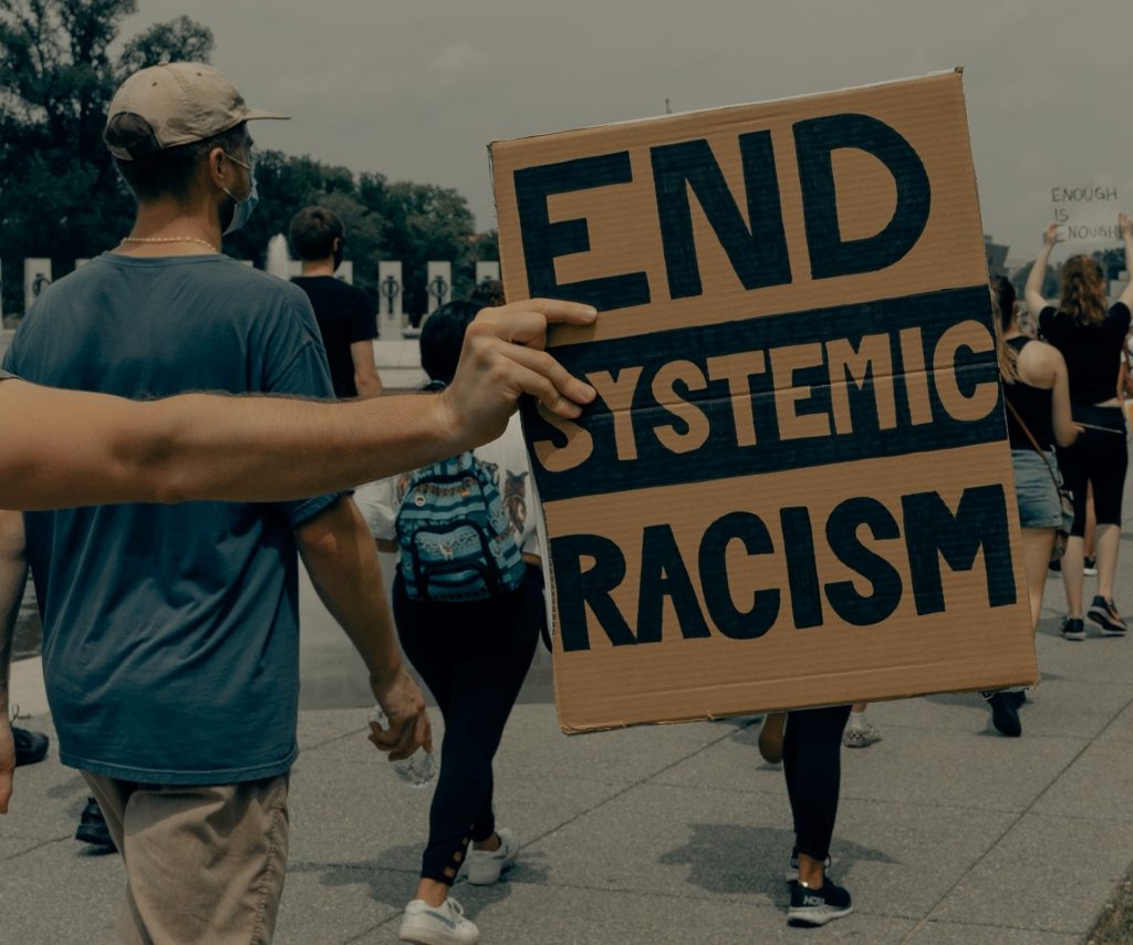 protestors marching, the image if focused on a placard that reads 'End Systemic Racism'