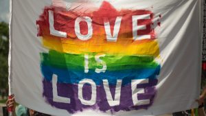 The words 'Love is Love' written on a white sheet painted over a rainbow flag