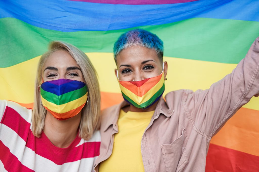 Couple celebrating pride while holding up the flag and wearing pride masks