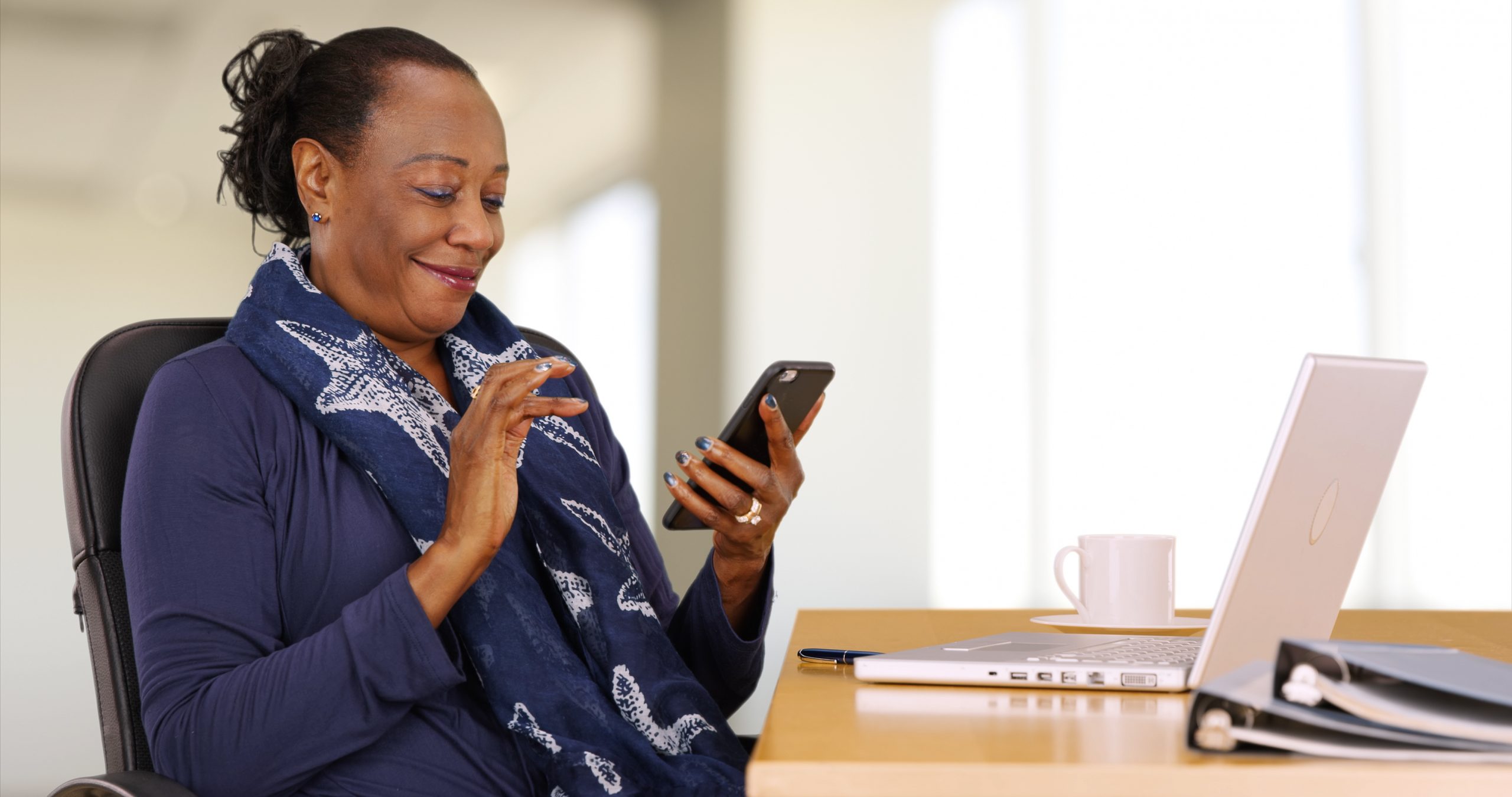 Older office woman at work desk communicating with colleagues via text message