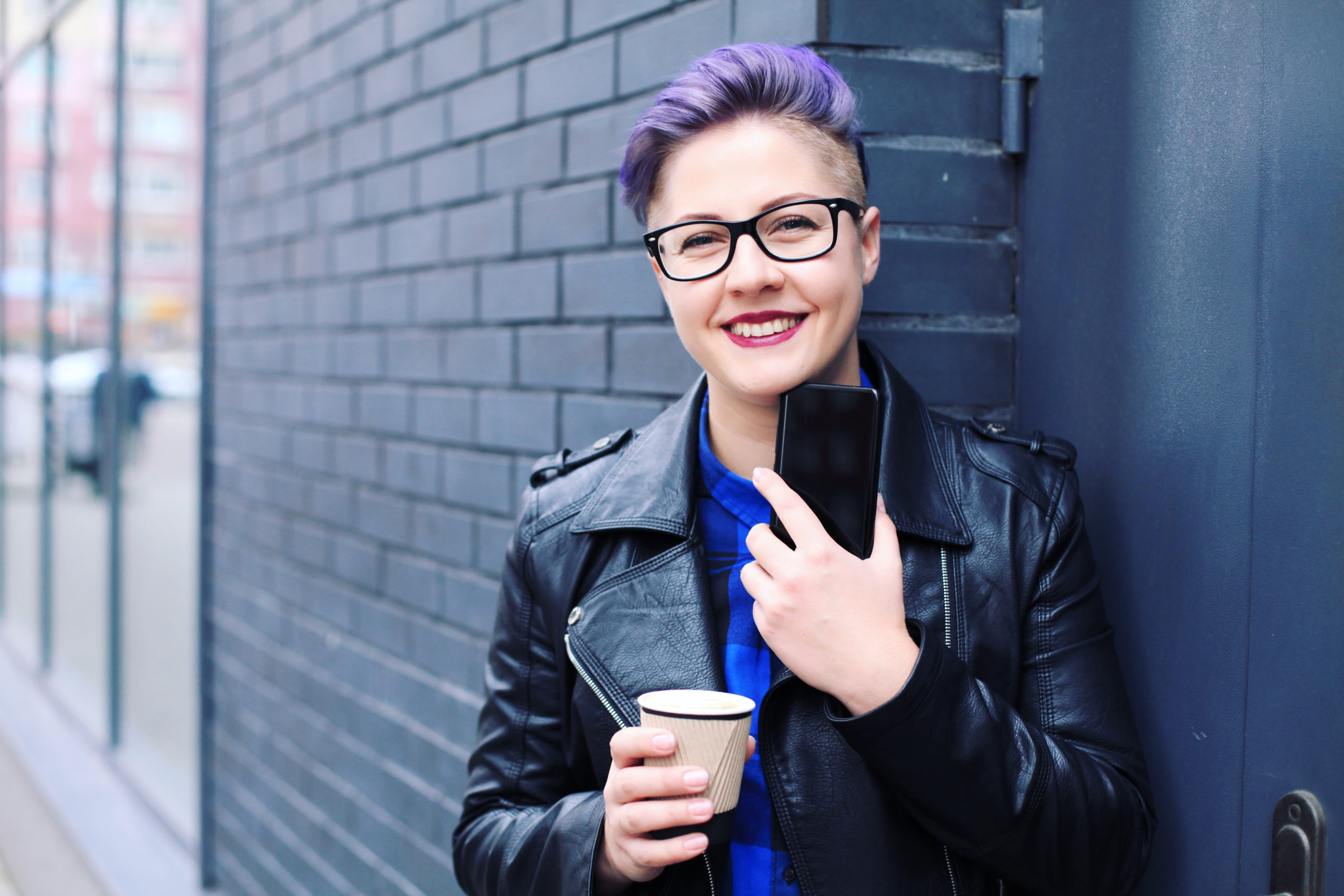 Trans person smiling at camera as they check their phone and have a coffee before work