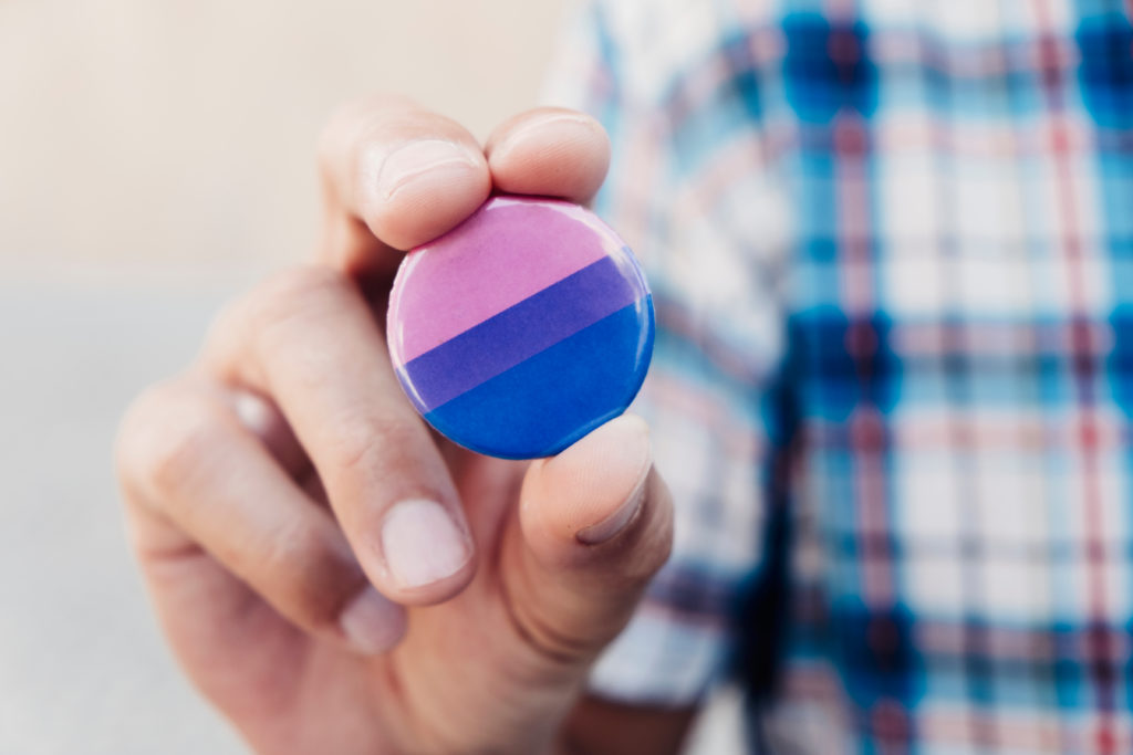 Close up of a hand holding a round bagde that displays the colours of the bisexual flag