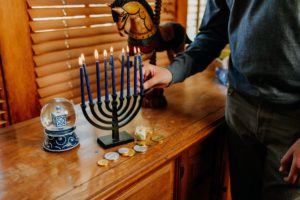 A side table with a menorah candleabra, a person's hand is in shot, lighting the candle