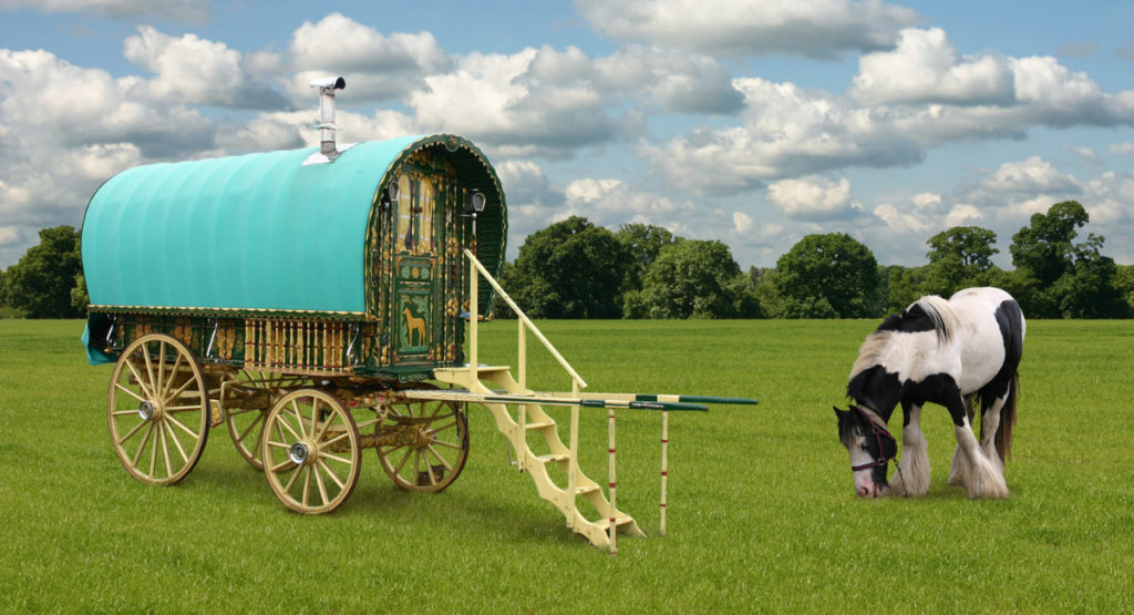 A traditional gypsy caravan in a grassy field, with a horse grazing nearby