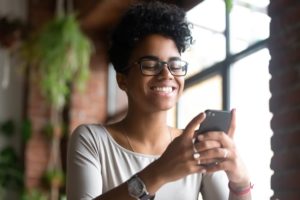 A person smiling, holding their phone in both their hands in front of them.