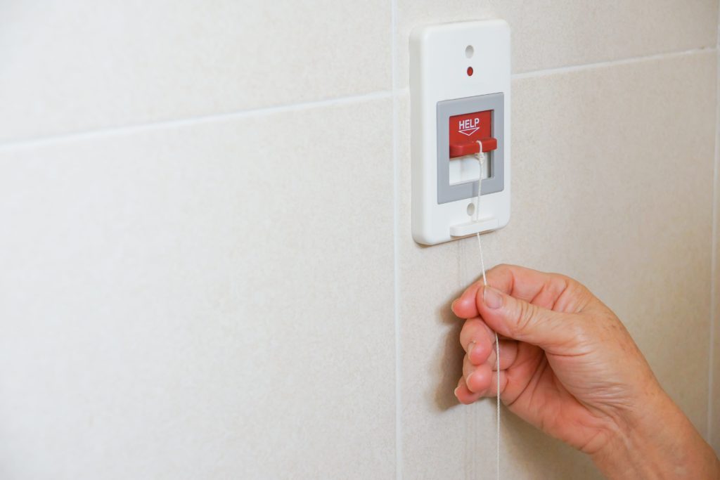 Close up of a person's hand pulling on a help cord against a tiled bathroom wall