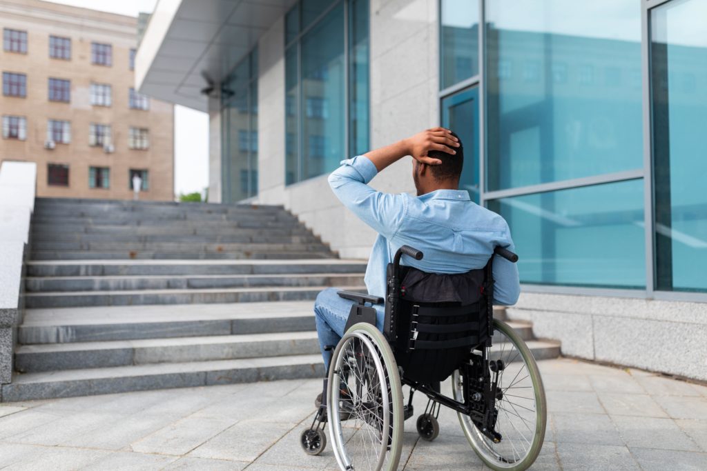 A person in a wheelchair at the bottom of a large set of steps - they are in distress about how they will get passed them.
