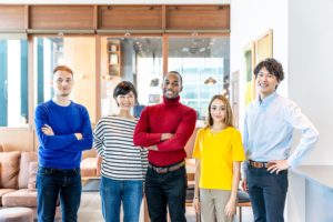 5 colleagues standing in a line smiling at the camera - they are in an office foyer and all represent different multi-racial identities