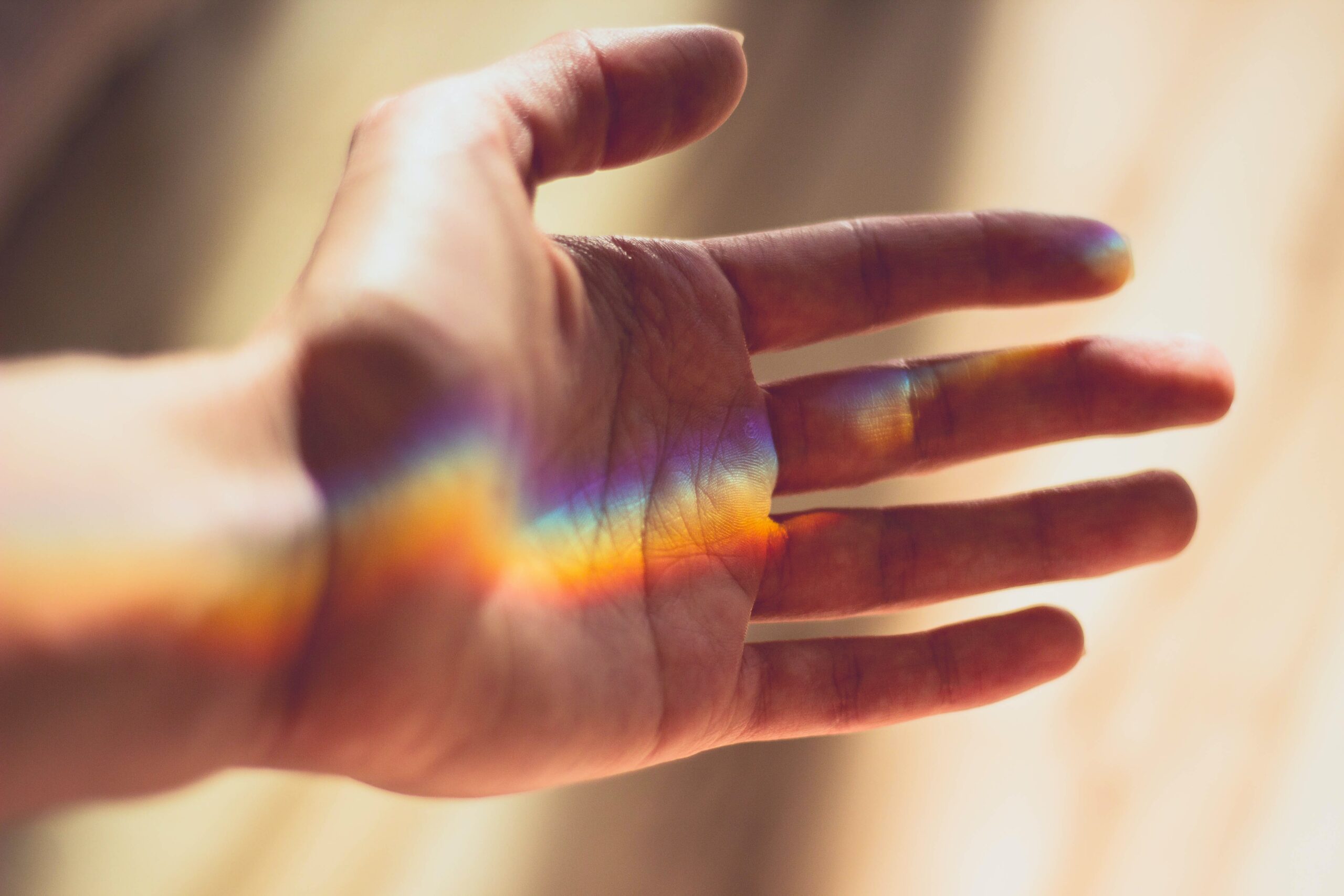 An outreached hand with rainbow light cast across it