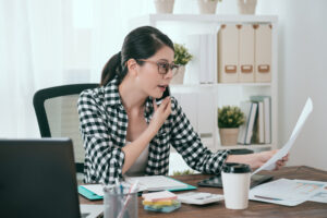 Office worker looking at documents in a busy office and having a discussion on the phone