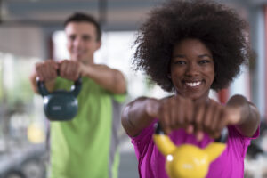 Two people lifting weights while smiling into the camera