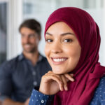 Business Women in a board meeting wearing a hijab smiling at the camera.