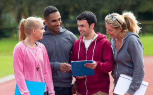 Four sports leaders on a track, hold clipboards and discuss their EDI training
