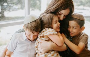 A modern Jewish mother embraces her three small children.