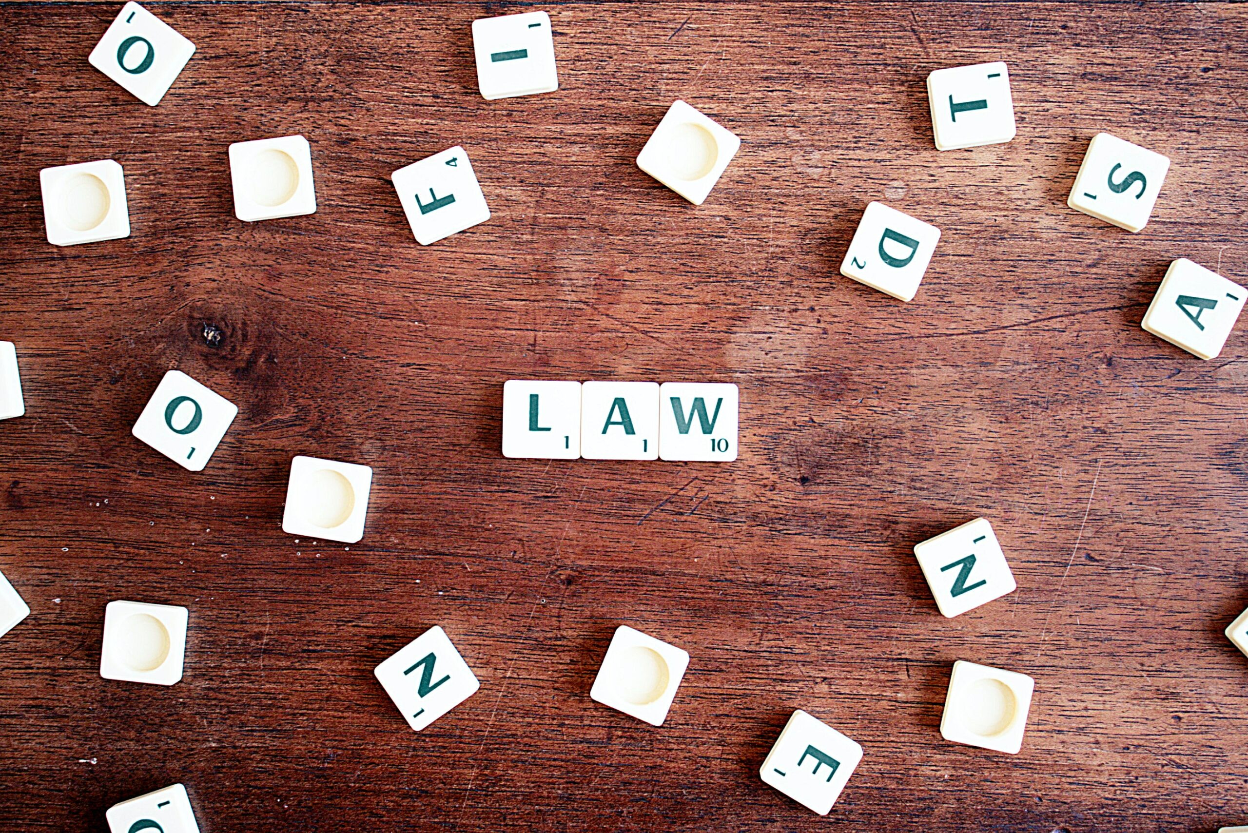 Scrabble tiles laid out on a brown wooden table with the word 'LAW' spelled out