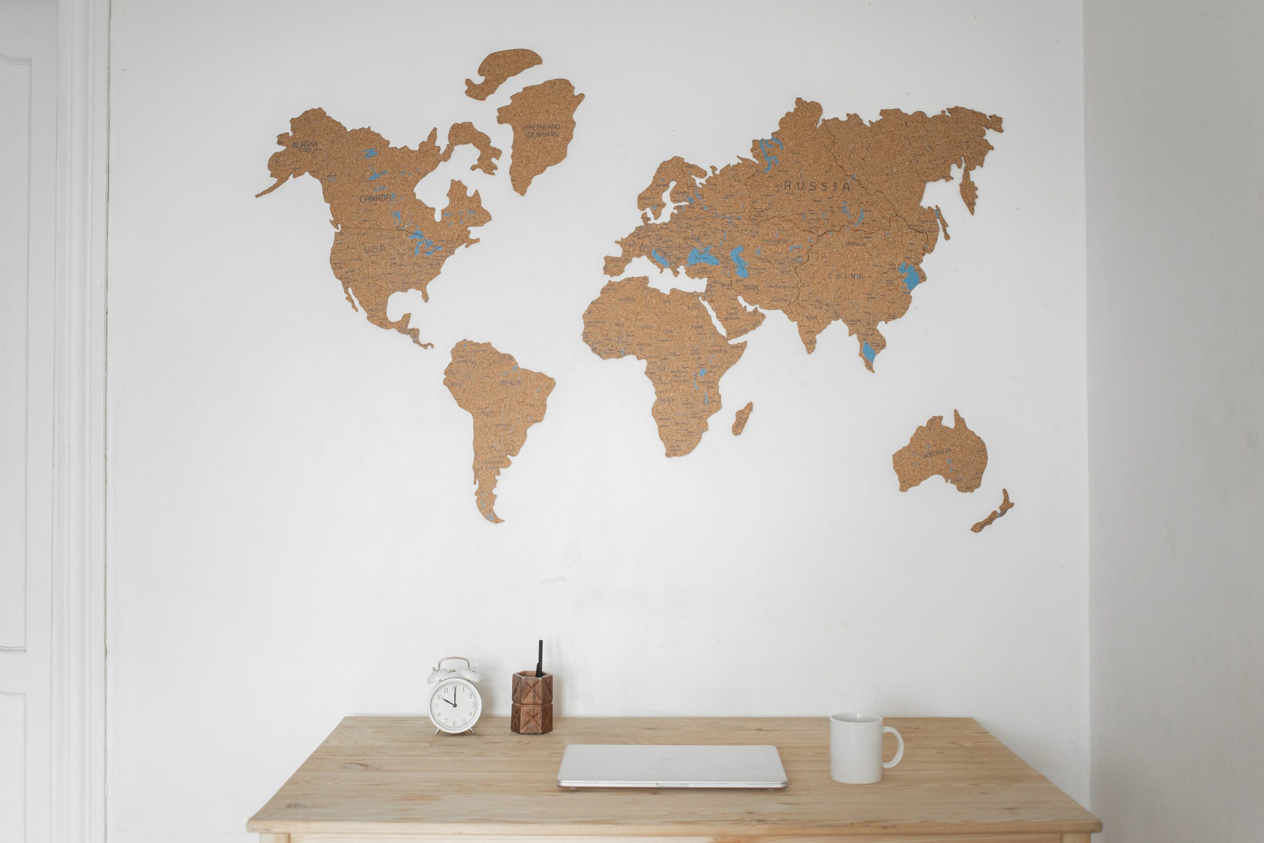 A cork map of the world posted onto a white wall with a desk below