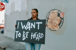A black woman holding a sign saying I Want To Be Heard.