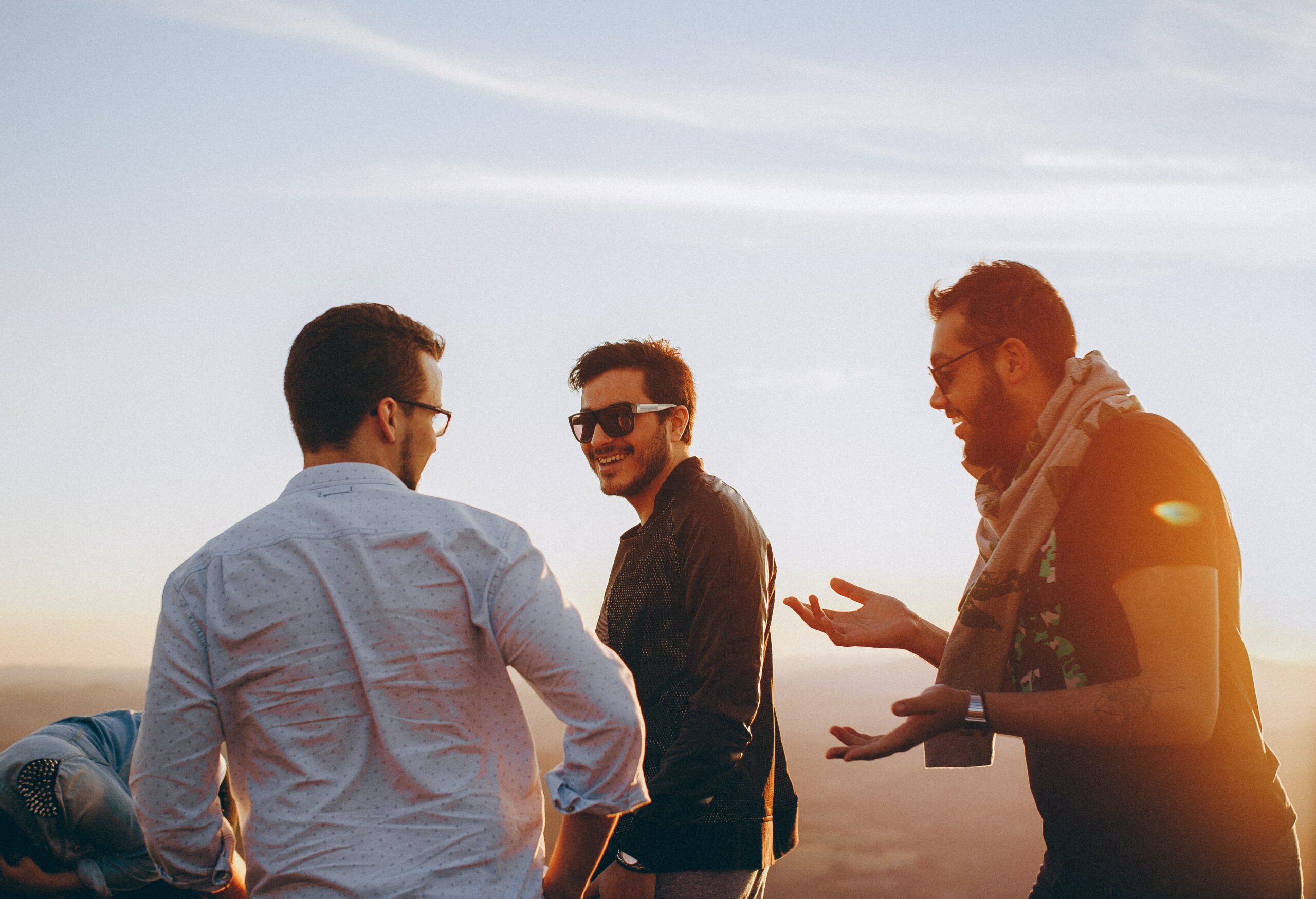 Three men looking happy as they talk together at sunset.