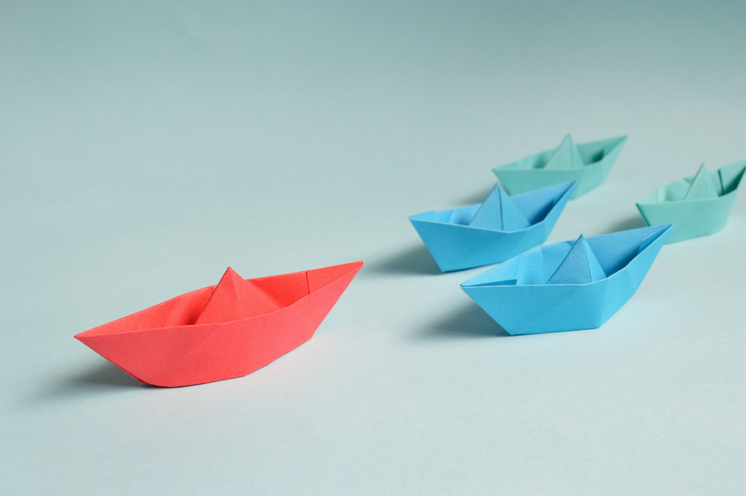 Blue paper boats being led by a red paper boat.