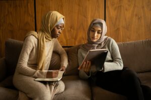 Two women with hijab or headcoverings on, reading from a tablet.
