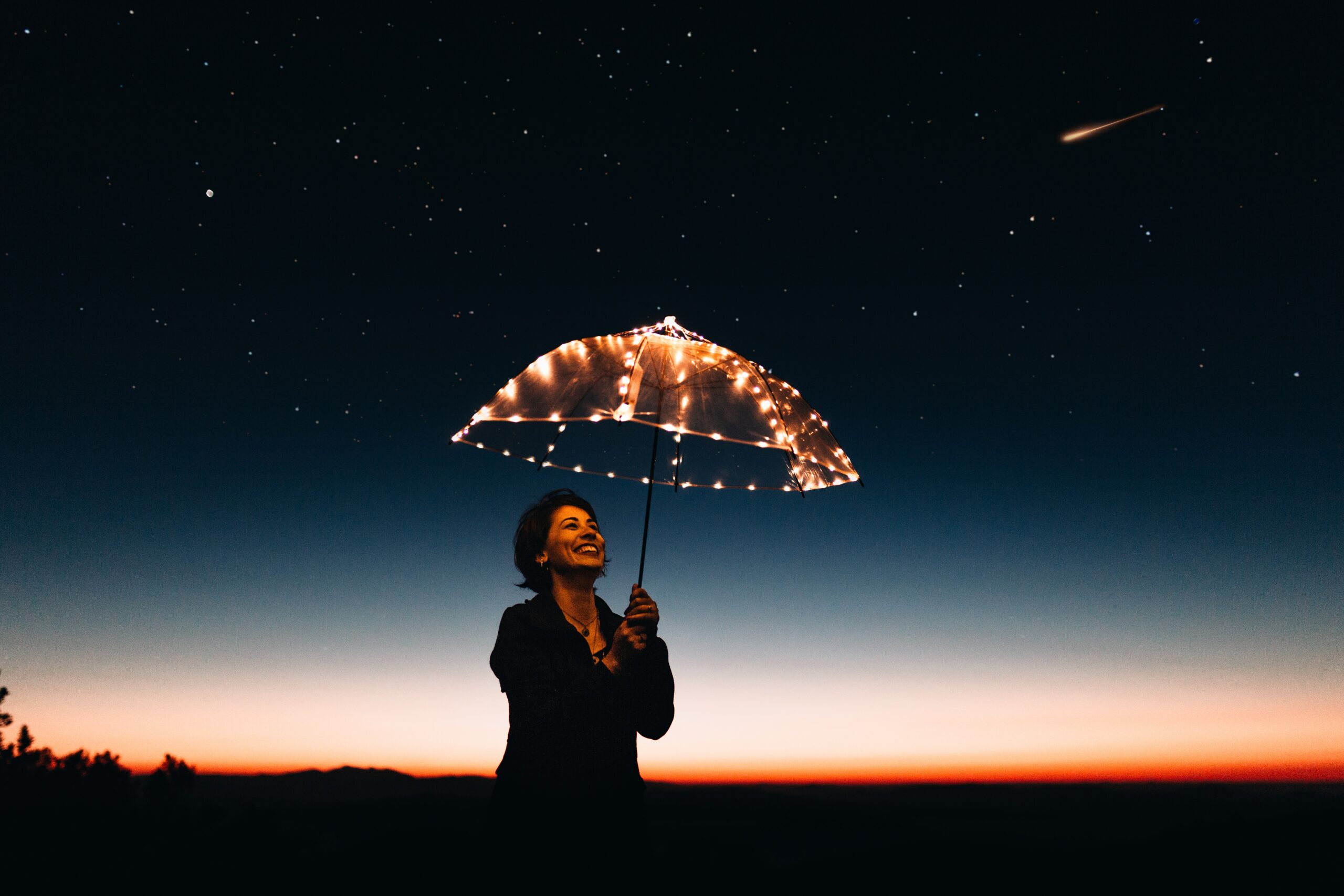 Woman with an umbrella made of lights standing against a sunset.