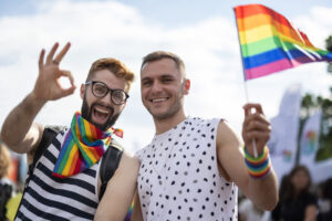 Pride Month 2023: two people celebrating pride as they take part in the march and wear rainbow coloured accessories and wave the pride flag