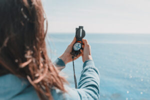 A person with long hair holding out an inclusion compass to guide their path. They are standing in front of the ocean.