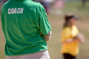 Close up shot of the back of a coach watching their team play, measuring the impact of EDI in Sport and Physical activity