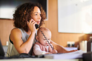 Working parent having a phone call in the office with their baby sat in their lap. The baby is playing with the phone chord.