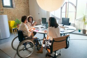 A wheelchair user and a person with a hidden disability chatting with their line manager in an open office