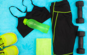 Work out shorts, top, shoes, weights and a green water bottle and towel laid out on a blue floor.
