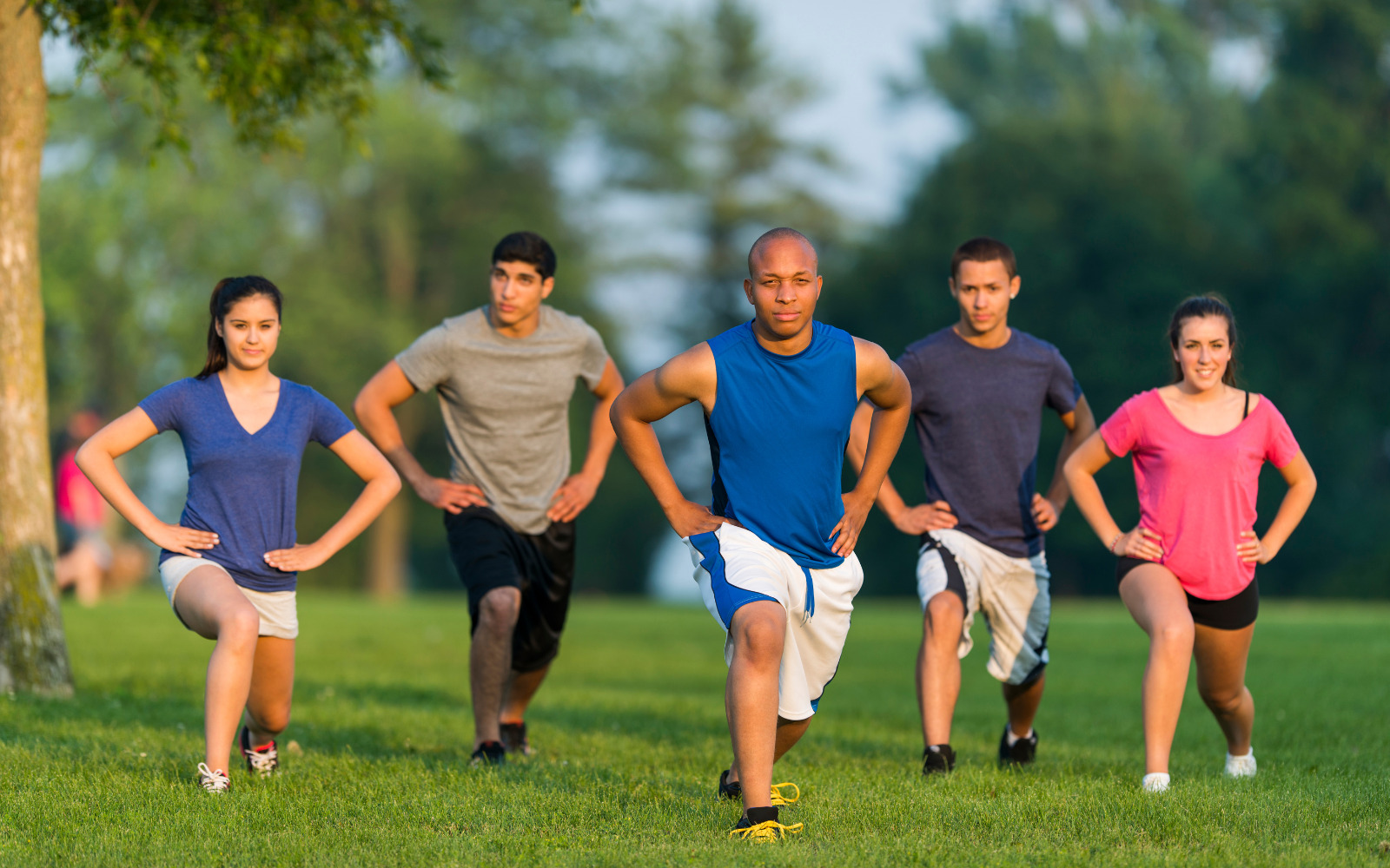 A group of people doing lunges in a park.