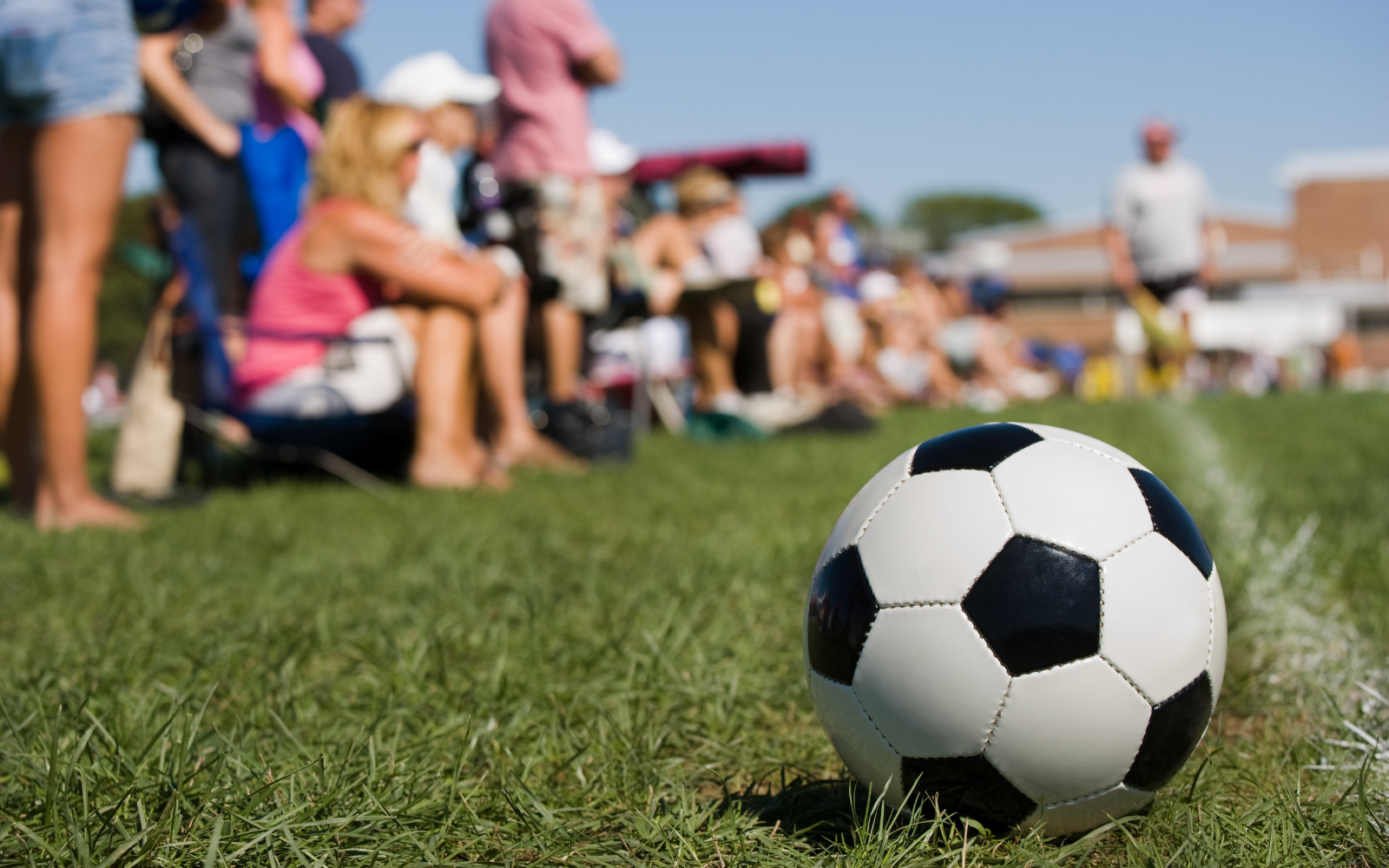 A football on a field with a group of people watching the game happening off screen in the background.