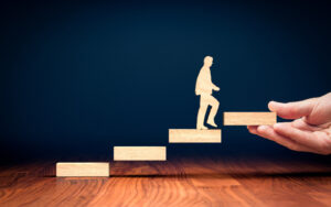A miniature cut-out human walking up some stairs being laid out by a human hand.