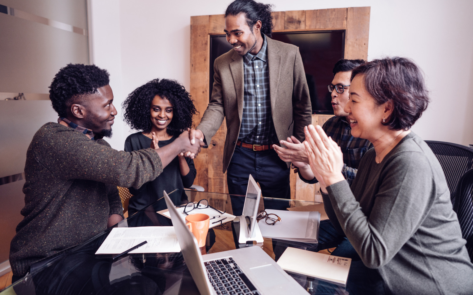 A group of seated people greeting a standing person who is shaking hands with one person at the table.