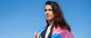 A trans person wearing the trans pride flag over their shoulders