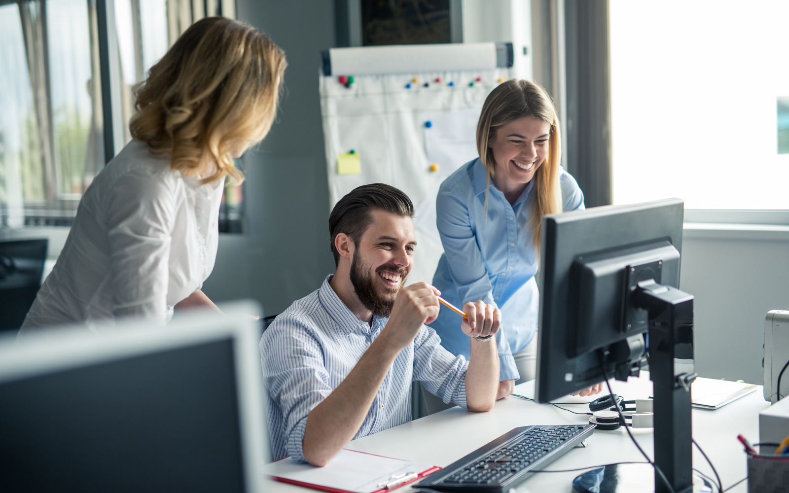 Three people in an office, looking at work and smiling