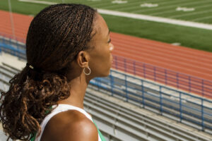A black female athlete stares pensively out at a running field