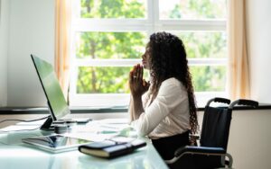 A black woman in a wheelchair praying at her desk.