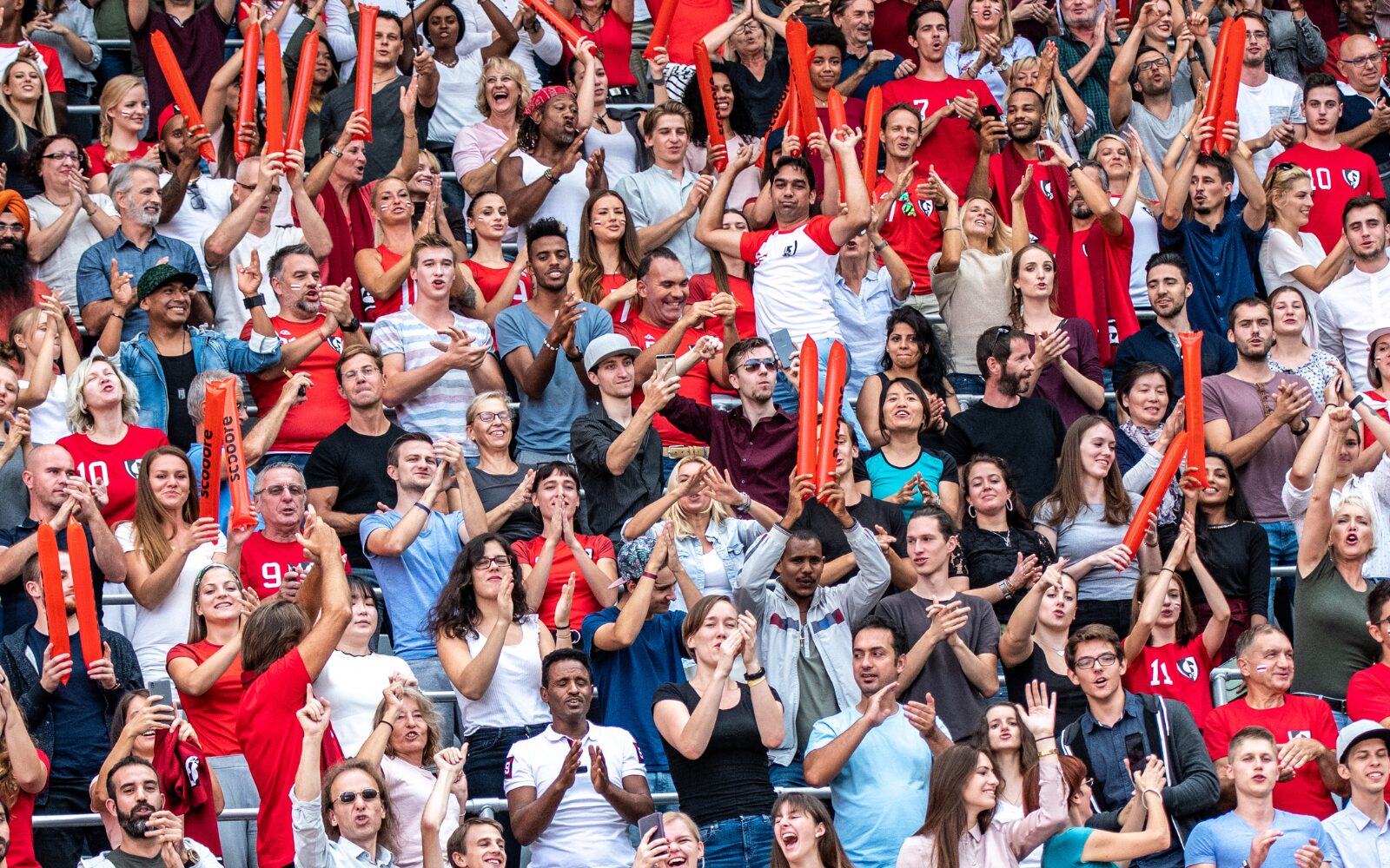 A diverse group of sports fans standing up and clapping their hands at a stadium event