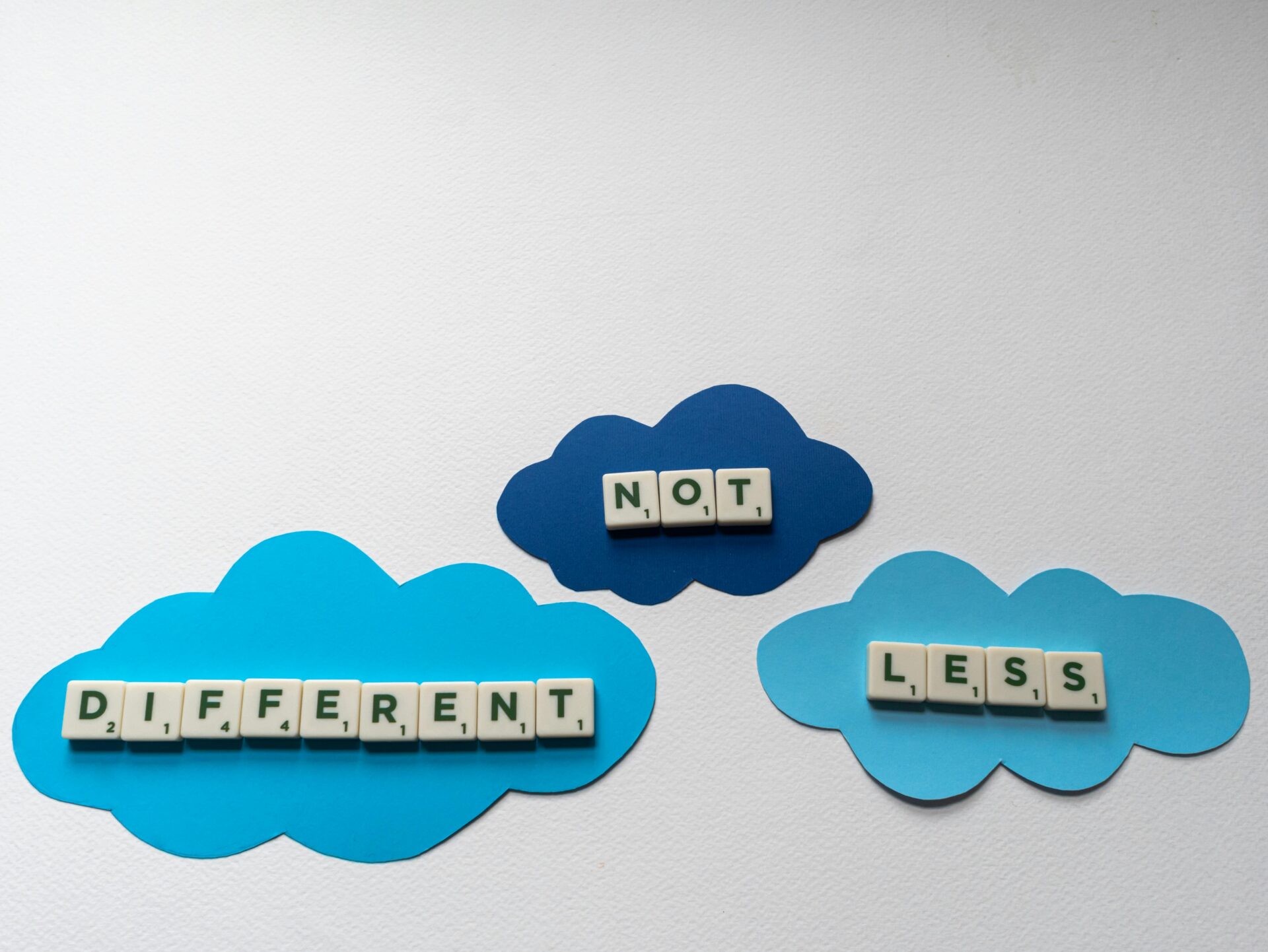 A photo of three blue clouds on a white background that spell out 'different not less'.