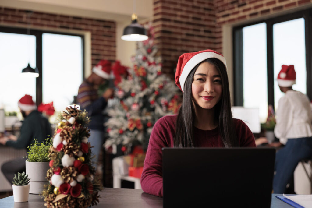 Portrait of business woman working in christmas season in startup office decorated with festive xmas ornaments and lights. Asian company worker using laptop during seasonal celebration