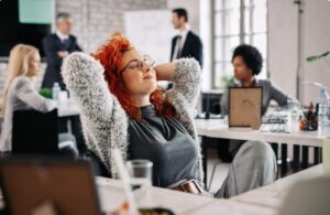Young creative businesswoman with hands behind head taking a break and resting with eyes closed in the office