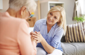 A woman sitting on a sofa and holding the hands with an elderly woman